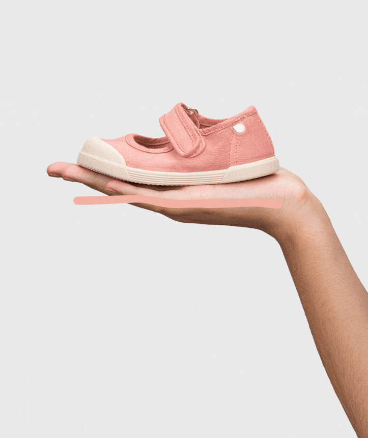 Sapato rosa claro de criança com fecho de velcro apoiado na mão