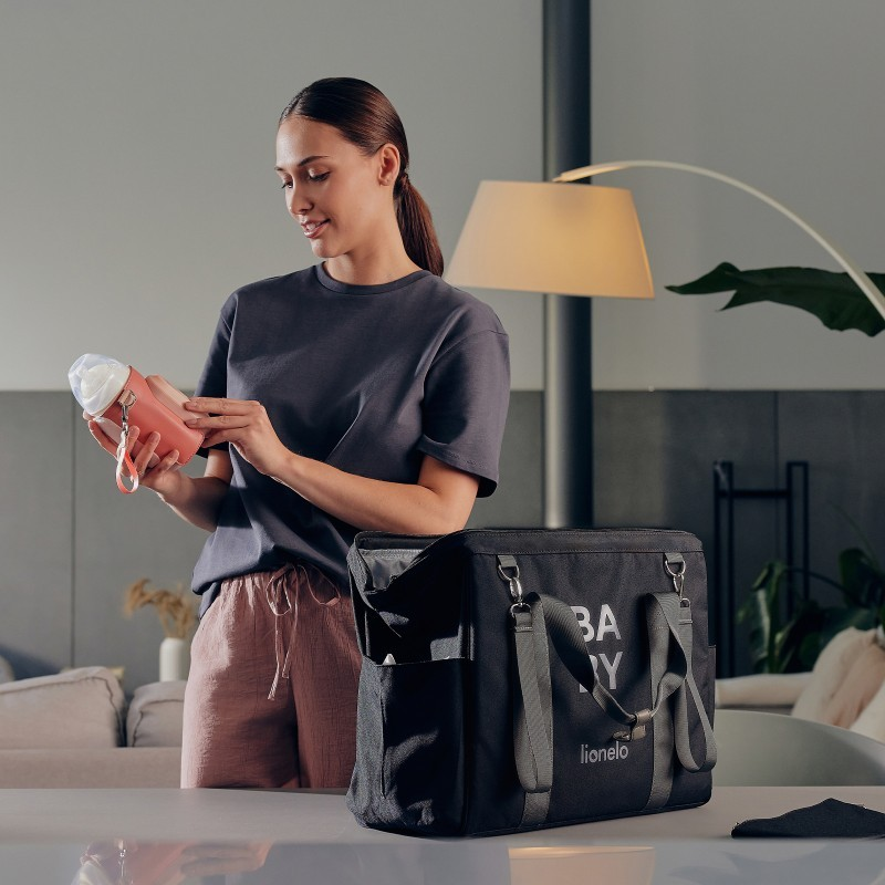 Mulher segura garrafa cor-de-rosa com bolsa preta 'BABY lionelo' num interior moderno