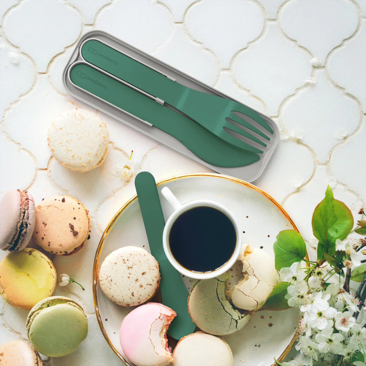 Conjunto de talheres verdes com estojo cinzento sobre superfície branca com macarons e chávena de café