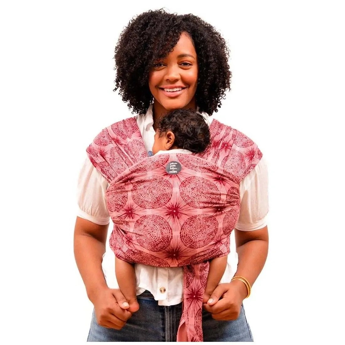 Porta-bebés vermelho com padrão circular usado para transportar bebê próximo ao peito.