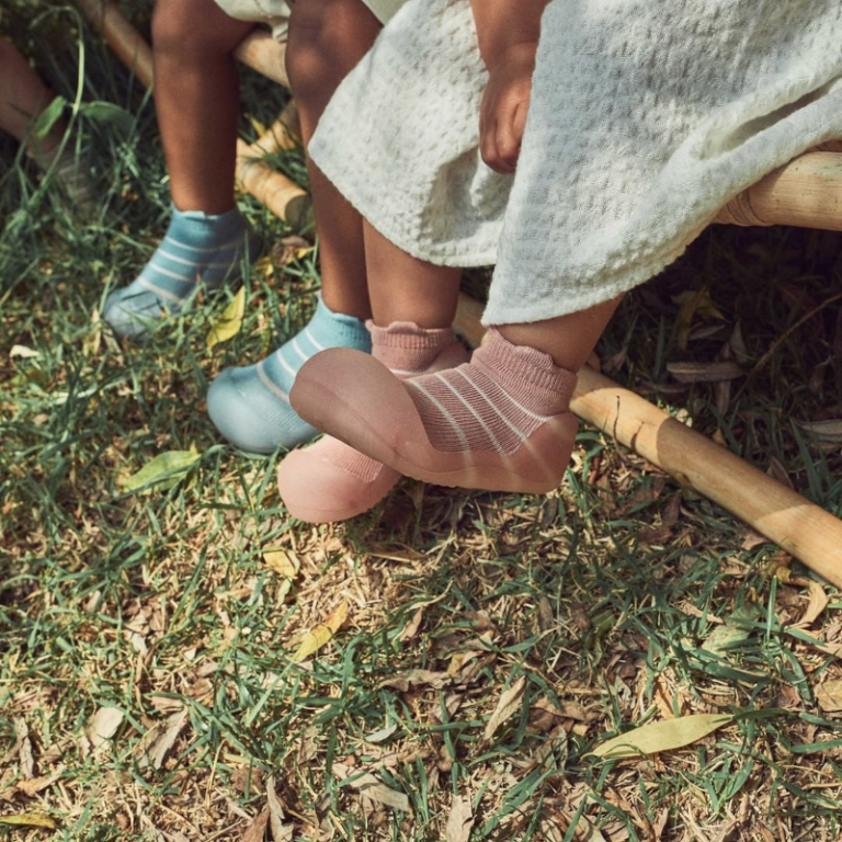 Meias de bebé rosa e azul com riscas, usadas por crianças sentadas ao ar livre.