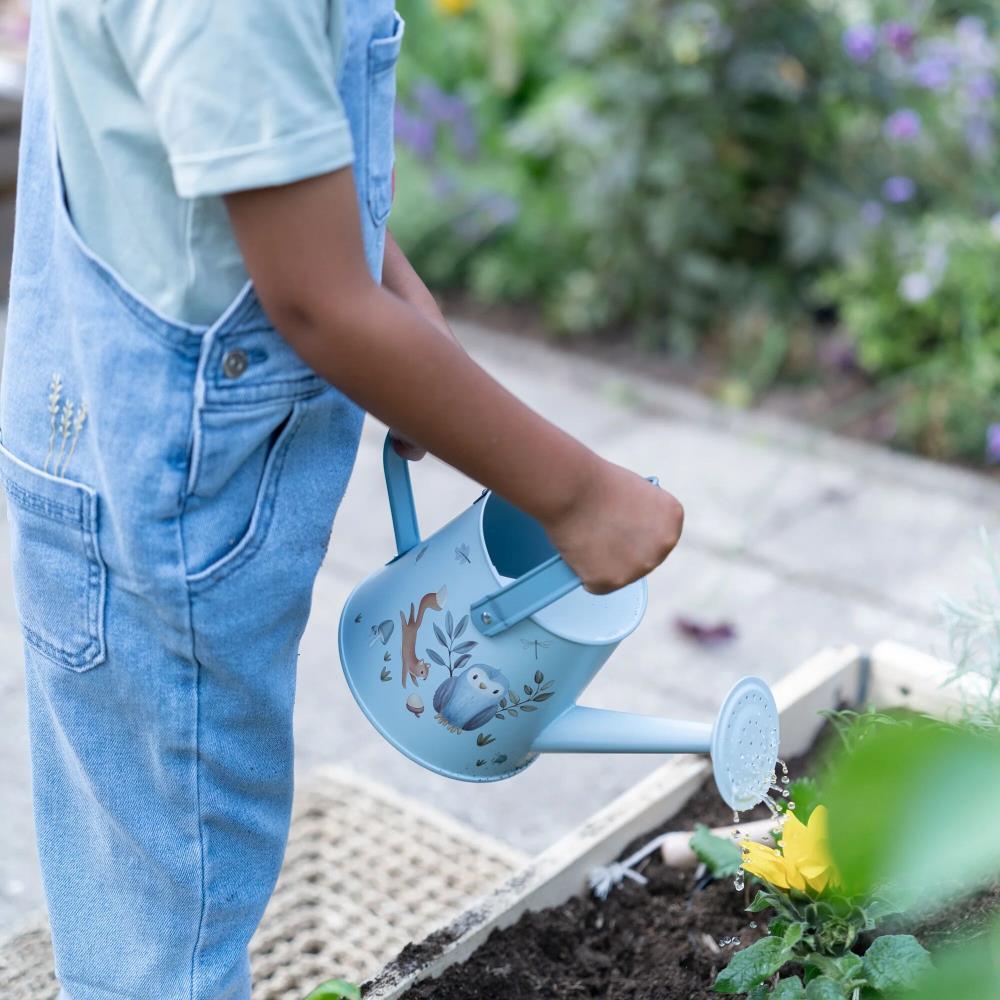 Criança a regar planta com regador azul claro decorado com ilustrações de animais.