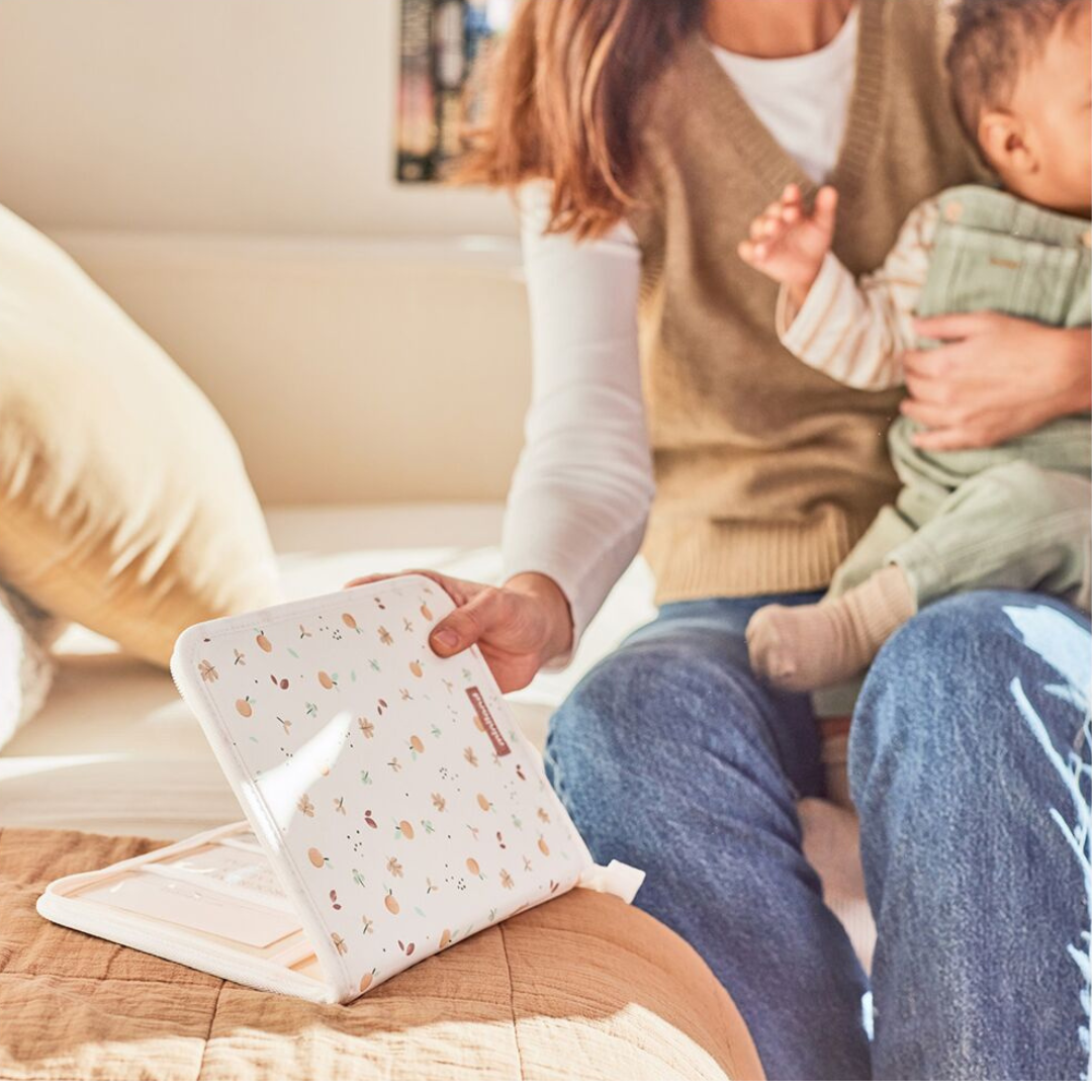 Carteira branca com padrão de frutas e folhas segurada por pessoa sentada numa cama.