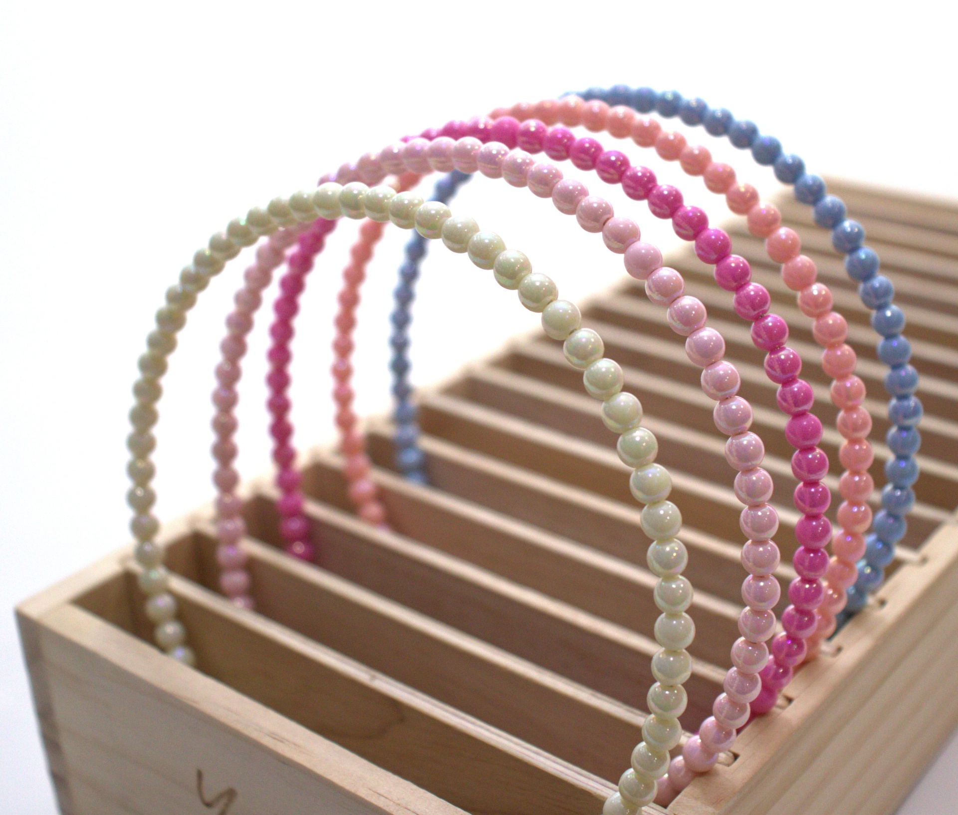 Cinco tiaras finas com pérolas falsas de cores diferentes numa caixa de madeira