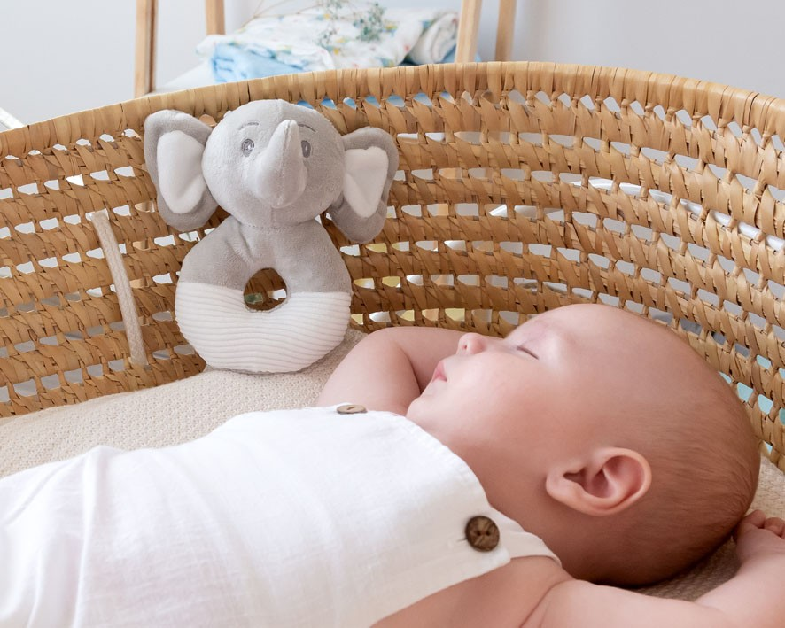 Bebé deitado em cesto com brinquedo elefante cinzento e branco de tecido