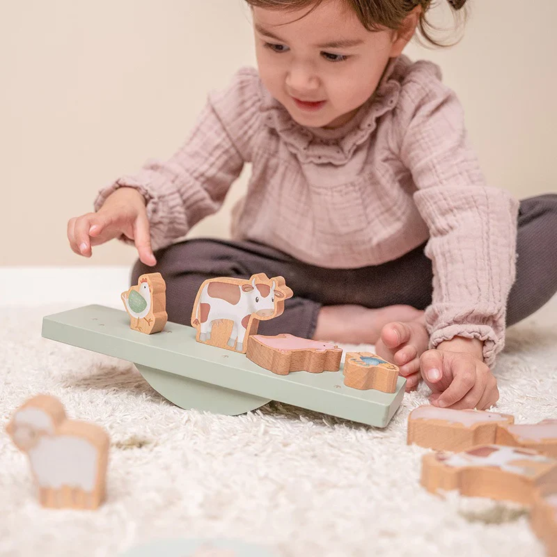 Brinquedo de equilíbrio em madeira verde com peças animais da quinta e criança a brincar no tapete
