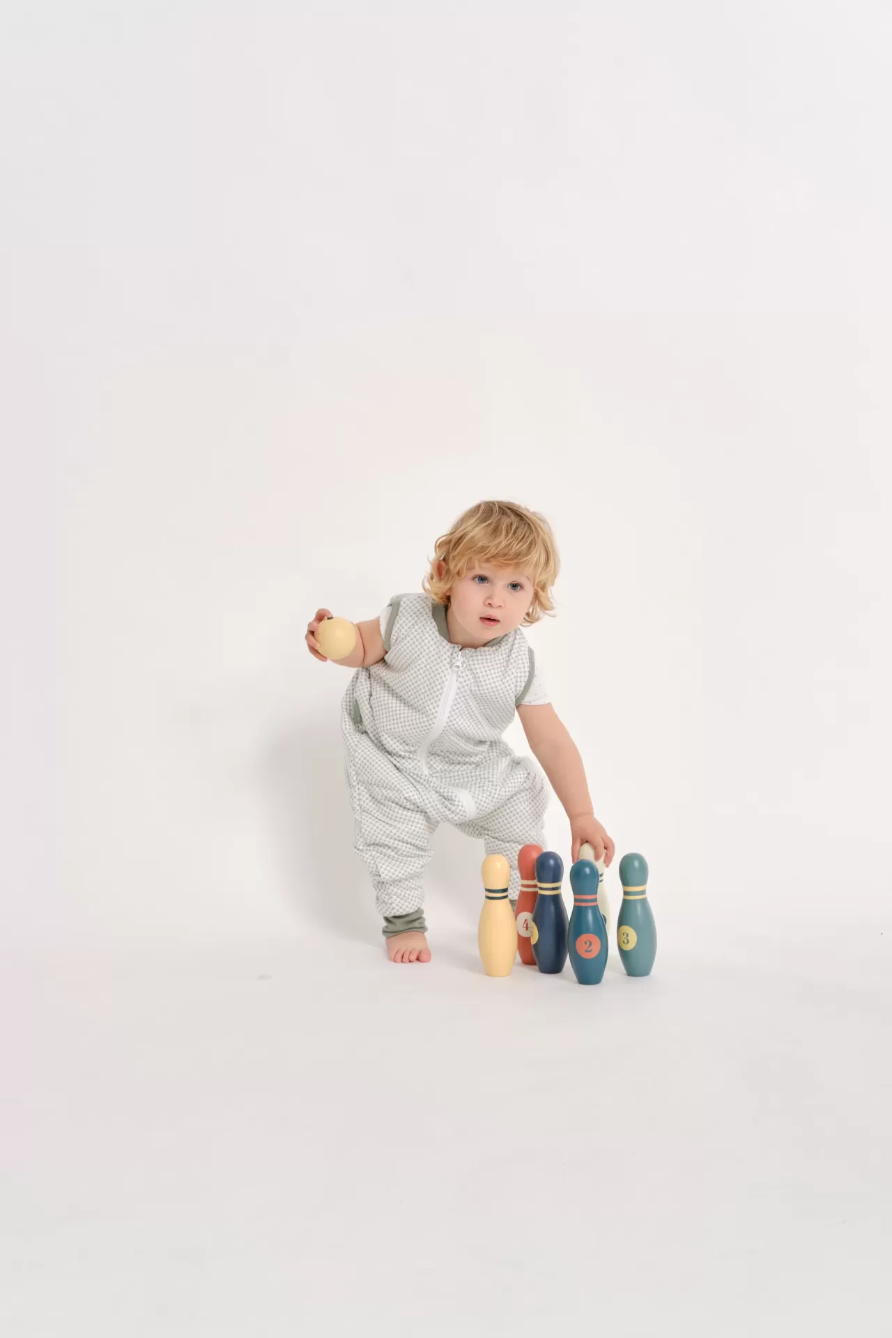 Criança com fato cinza a brincar com pinos de bowling de madeira numerados