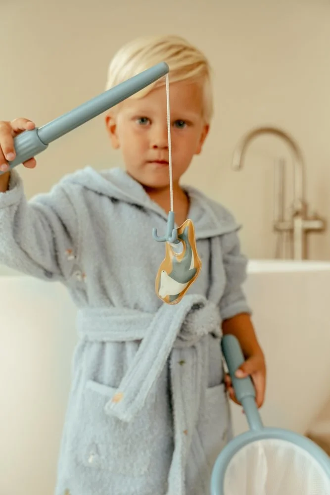 Criança com roupão azul claro segurando vara de pesca de brinquedo com peixe e rede azul claro