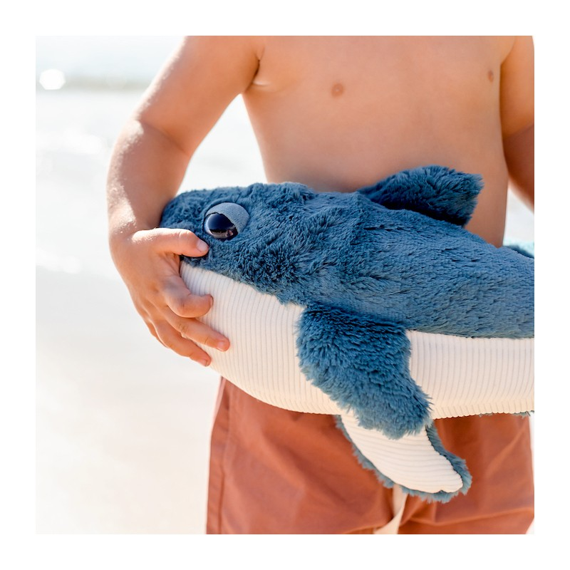 Pelúcia de tubarão azul com barriga branca segurada por criança na praia