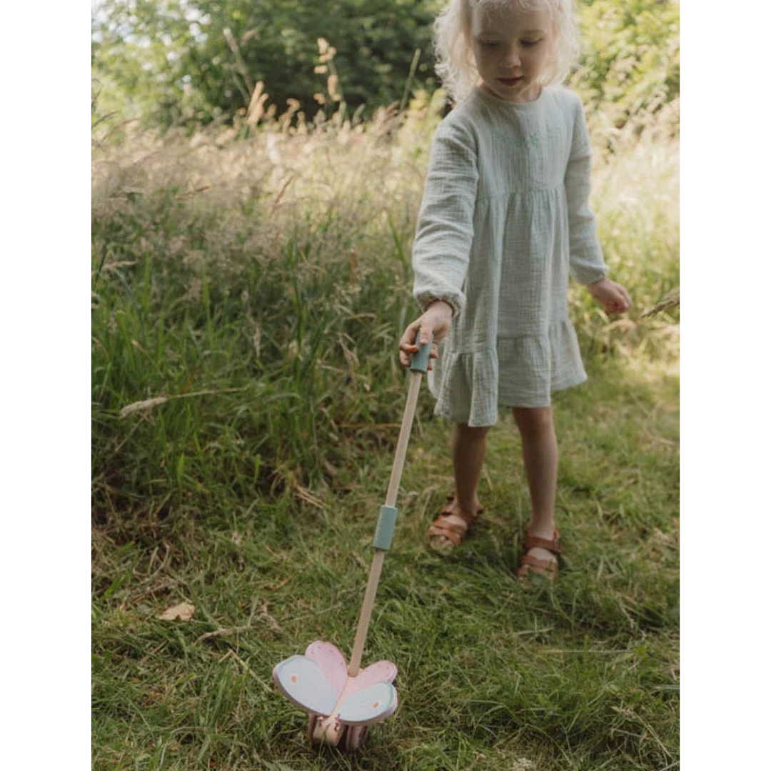 Criança com vestido branco segurando brinquedo de empurrar em forma de borboleta na relva
