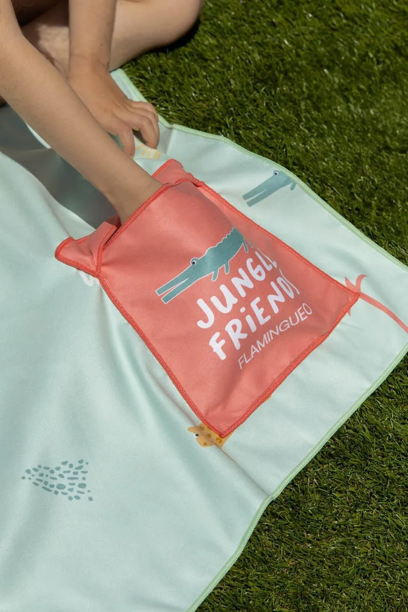 Manta azul clara com bolsa cor-de-rosa com desenho de crocodilo e texto JUNGLE FRIENDS FLAMINGUEO sobre relva