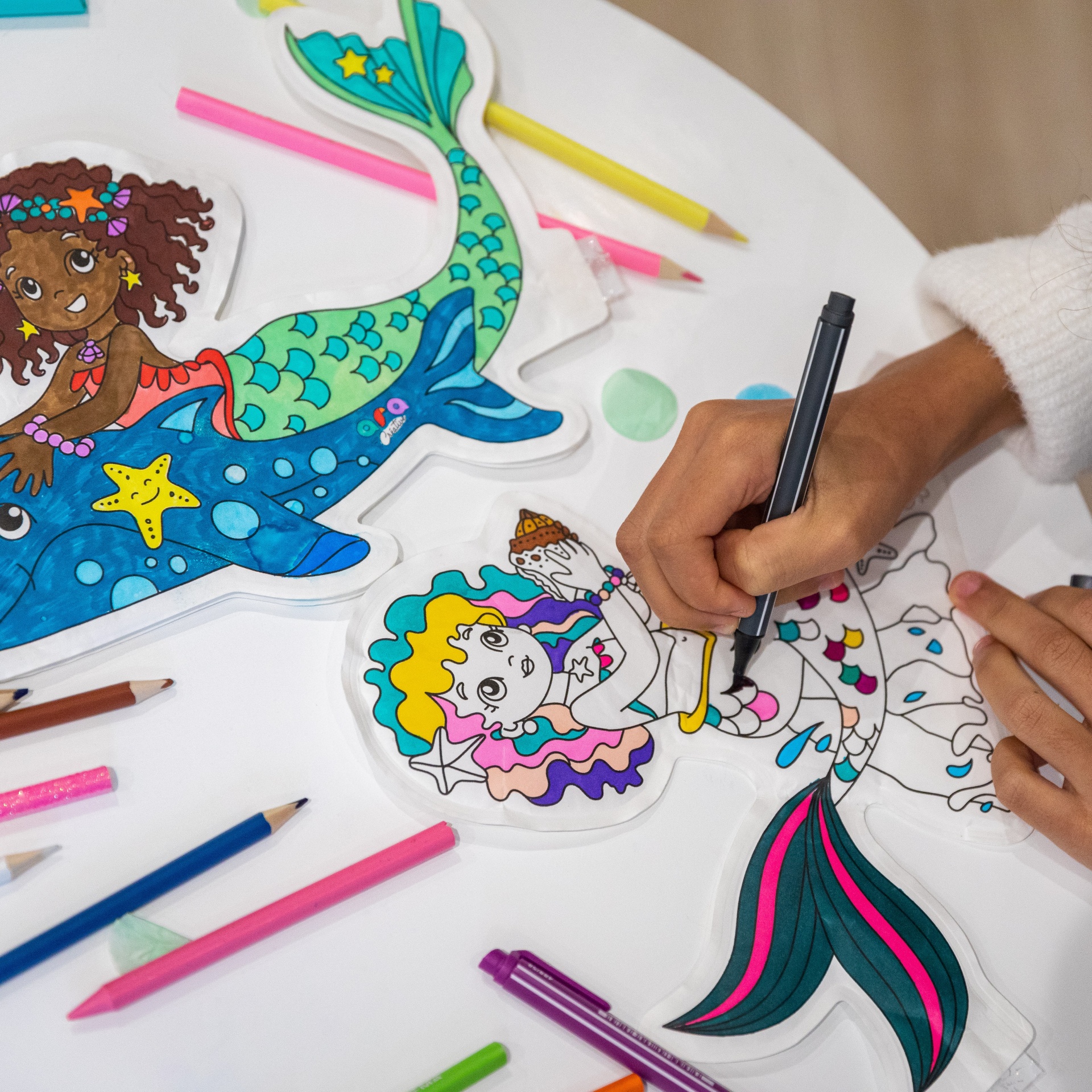 Duas figuras de sereias para colorir com lápis de cor e canetas na mesa