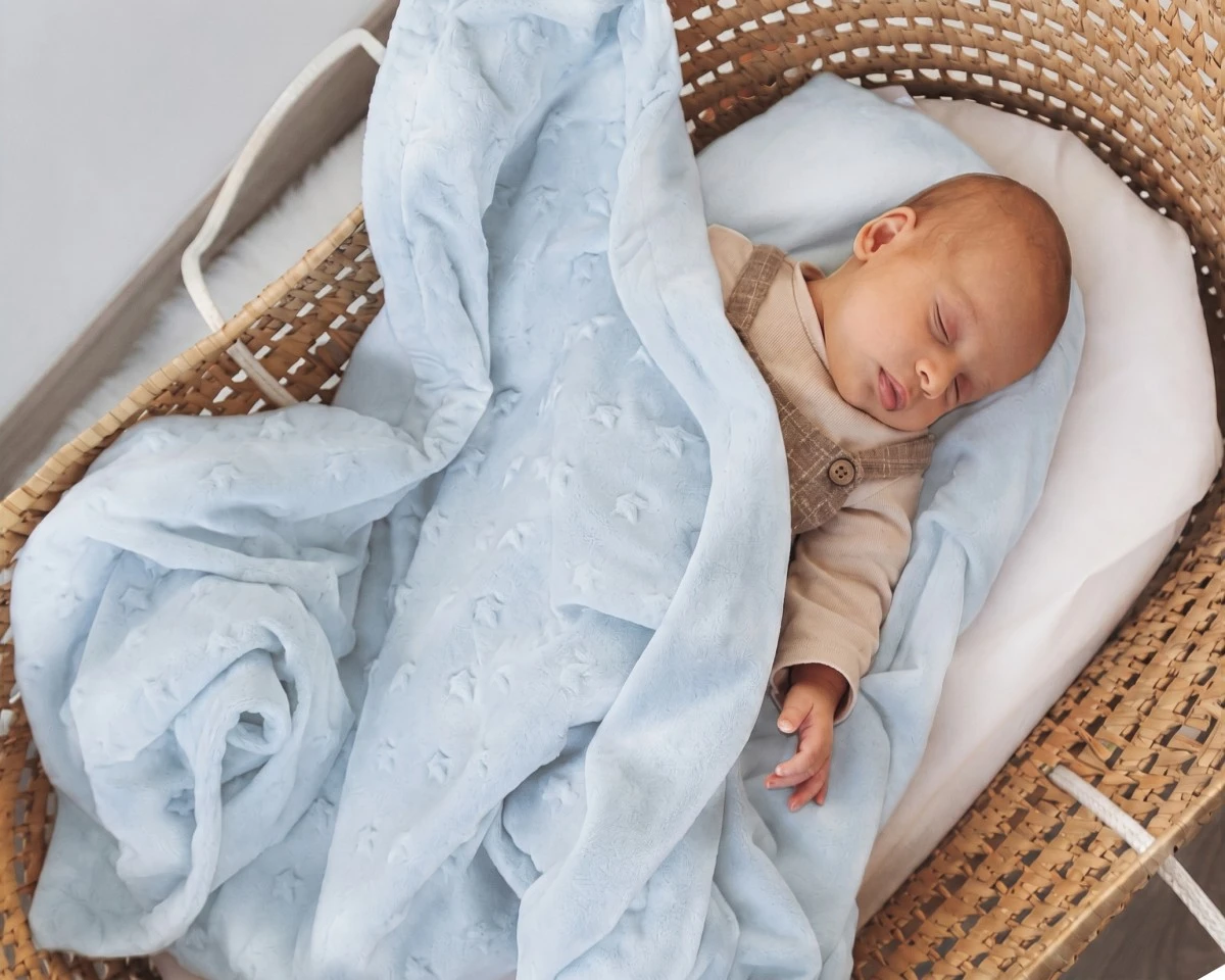 Bebé dormindo numa cesta de vime com manta azul clara texturizada e colchão branco