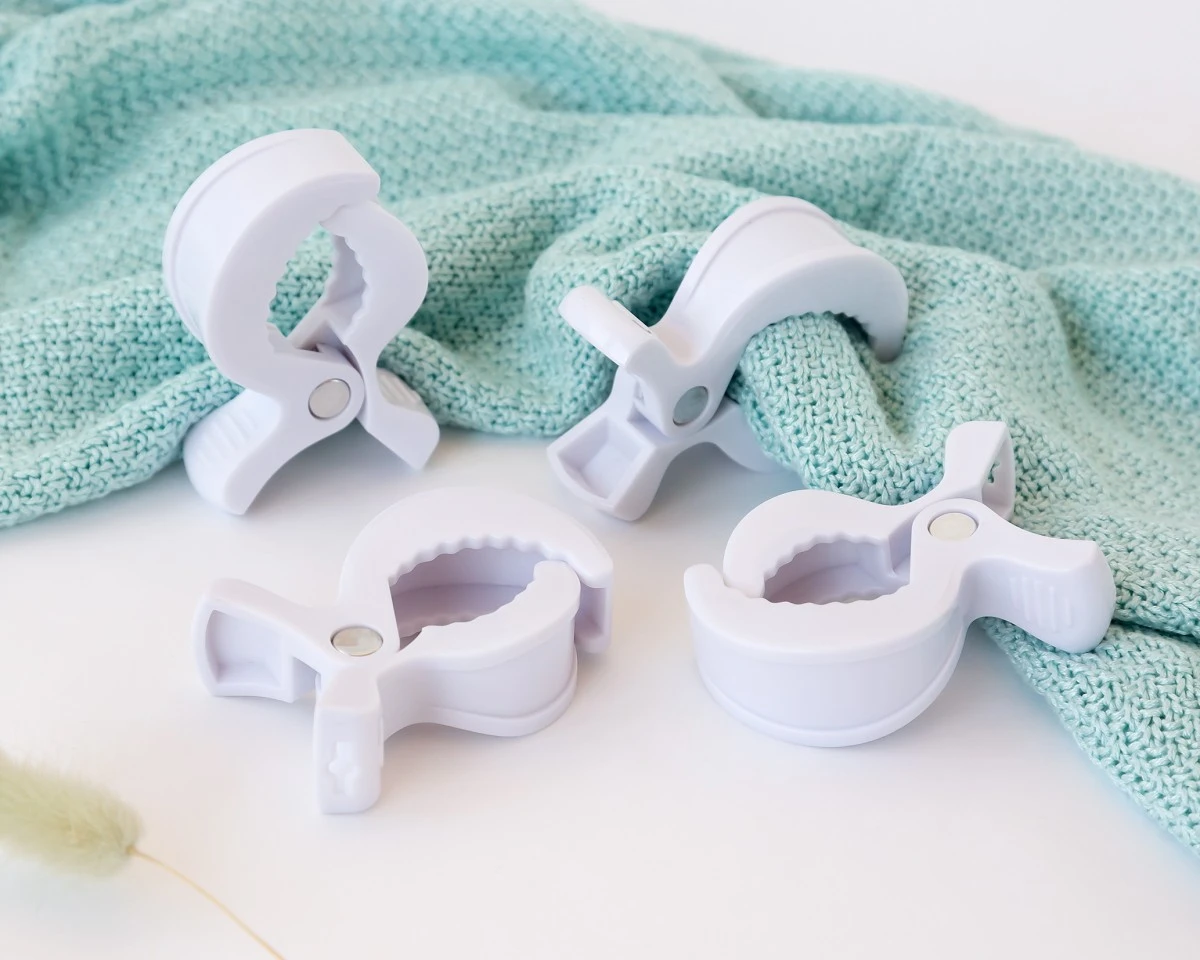 Quatro pregadores brancos de plástico com interior serrilhado sobre superfície branca e tecido azul claro