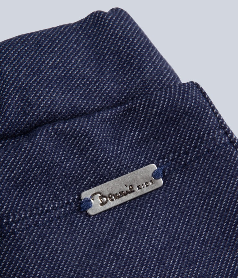 Etiqueta metálica com texto Benetto KIDS em roupa azul escura com textura canelada