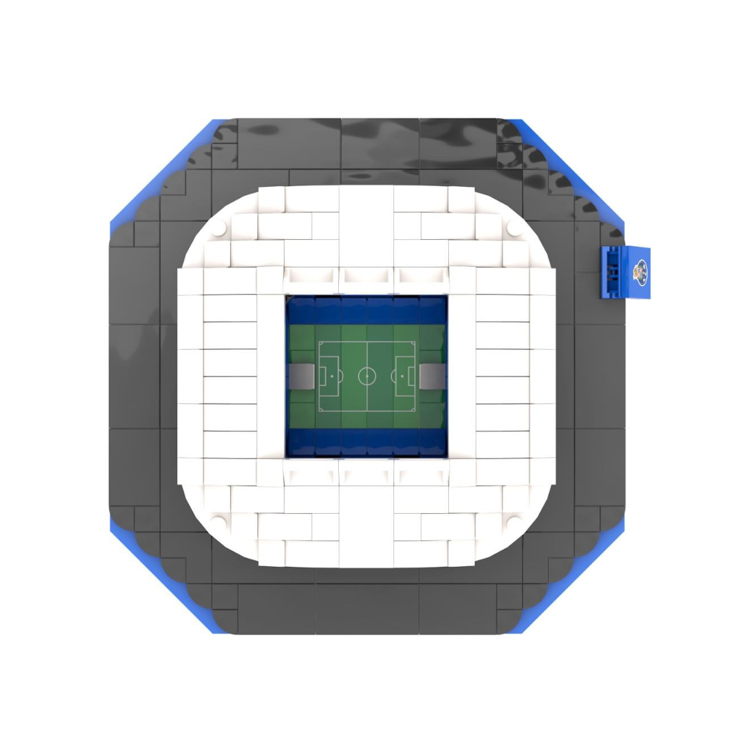 Miniatura de estádio de futebol feita com blocos de construção tipo Lego com arquibancadas brancas e campo verde.