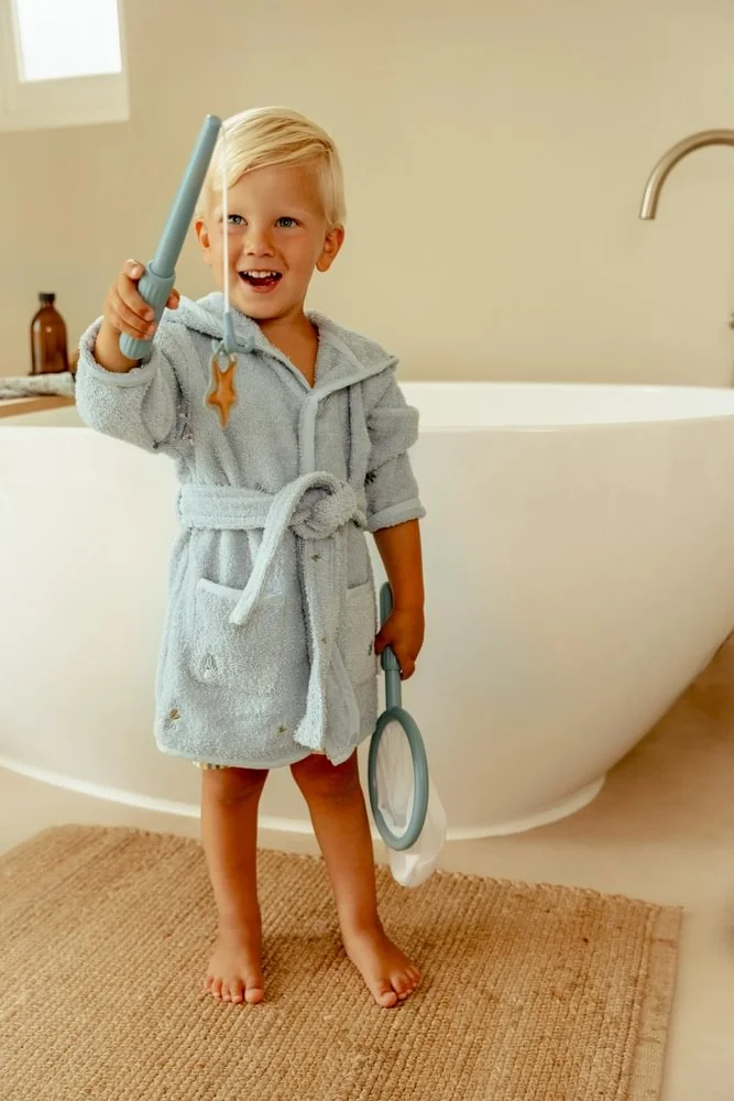 Criança com roupão cinza e varas azuis em casa de banho