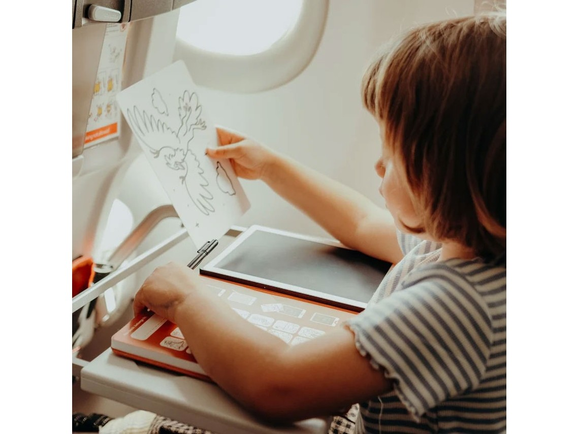 Criança num avião com dispositivo electrónico e livro de colorir