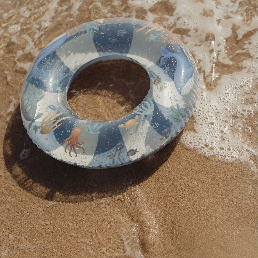 Bóia insuflável azul e branca com desenhos marinhos na areia molhada da praia