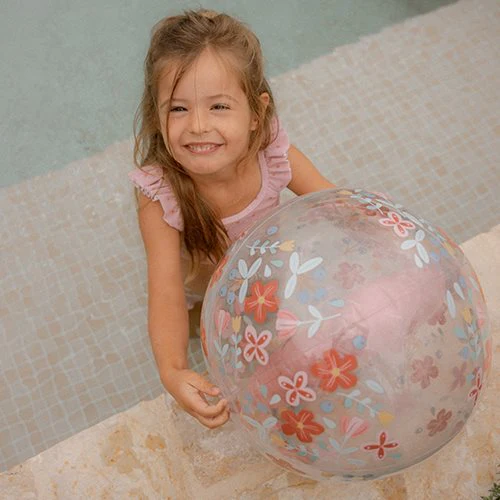 Menina com bola de praia transparente com flores coloridas junto a piscina