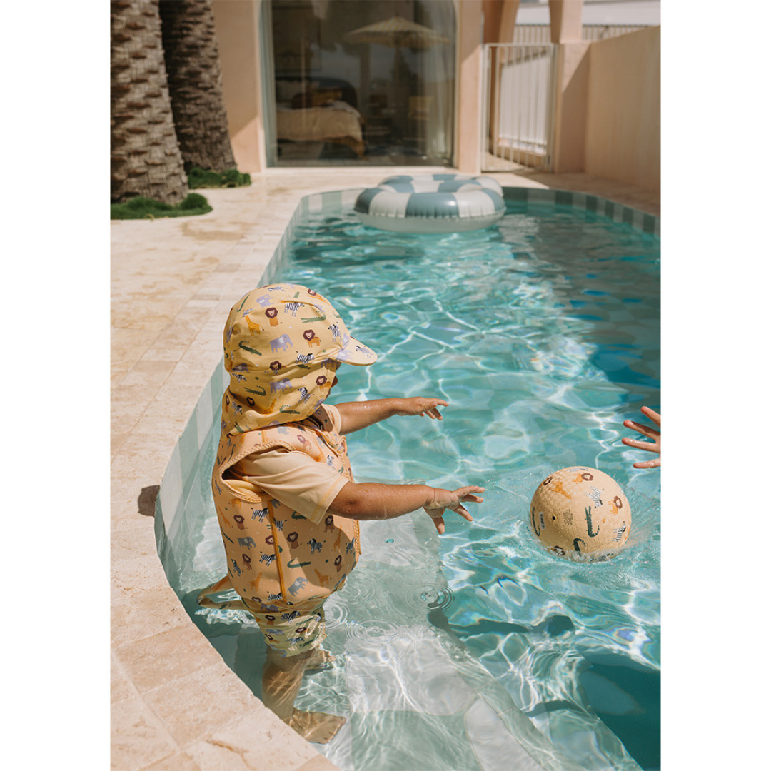 Criança com roupa de banho amarela com padrão de animais numa piscina a brincar com bola