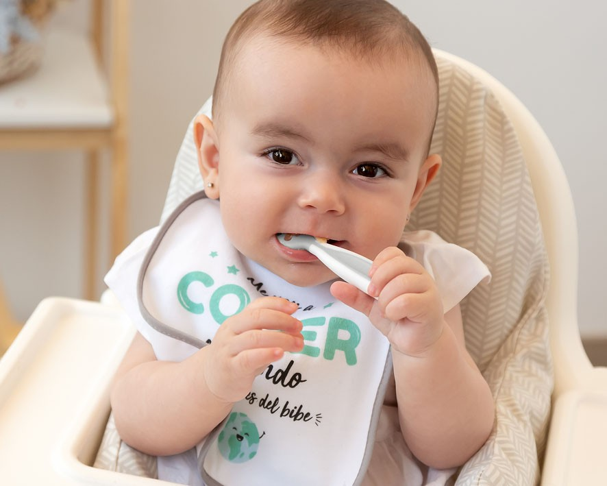 Bebé em cadeira de refeição com babete escrito Comer é do bebé