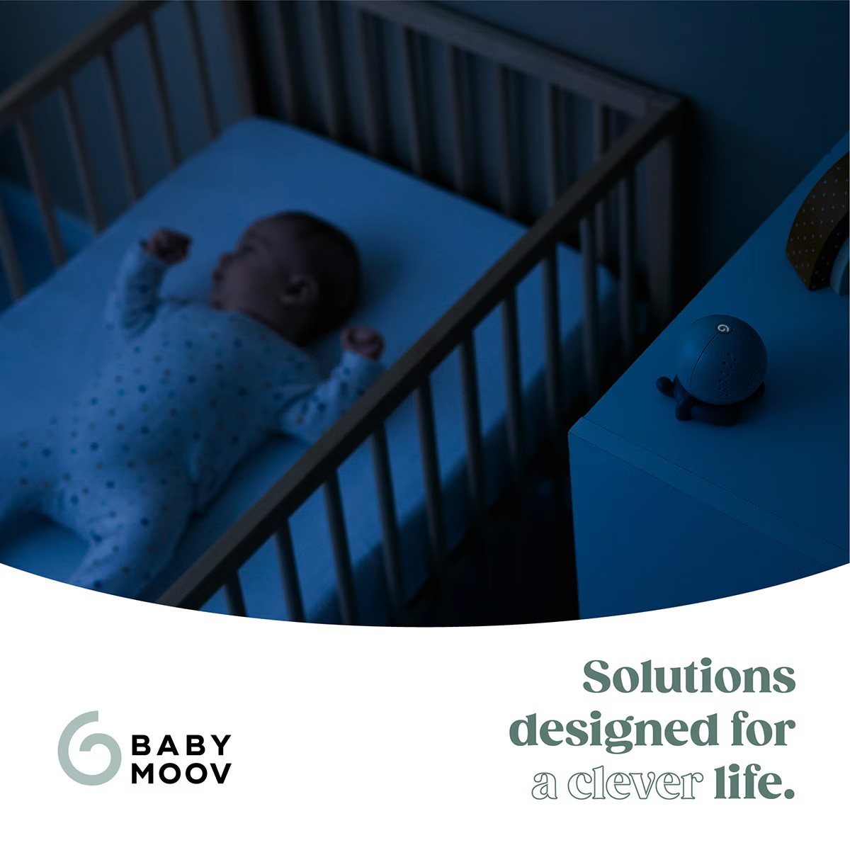 Berço com bebé a dormir e dispositivo esférico azul numa mesa ao lado