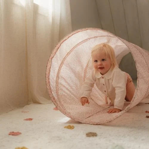 Criança engatinhando em túnel de brincar rosa claro com padrão floral