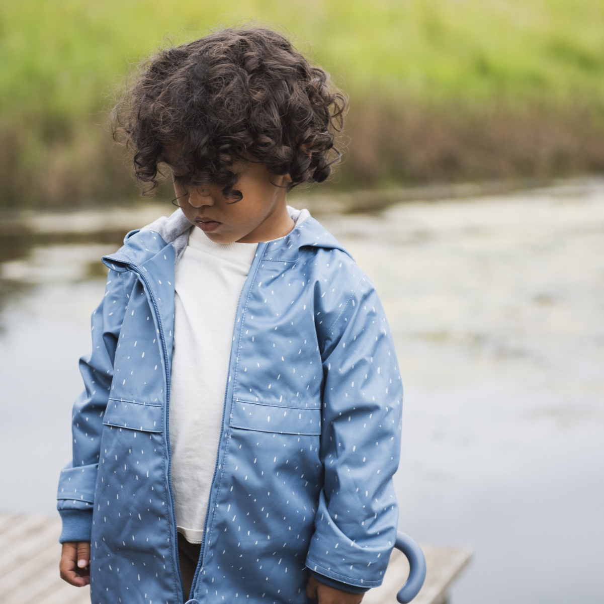criança com casaco azul claro e guarda-chuva azul perto de água