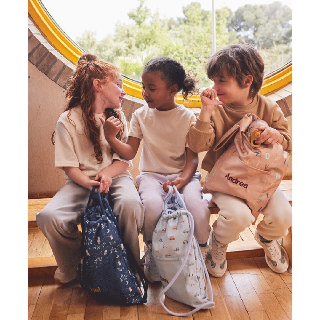 Três crianças sentadas com mochilas personalizadas sob uma janela redonda