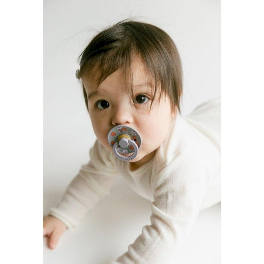 Bebé com chupeta cinzenta colorida numa superfície branca