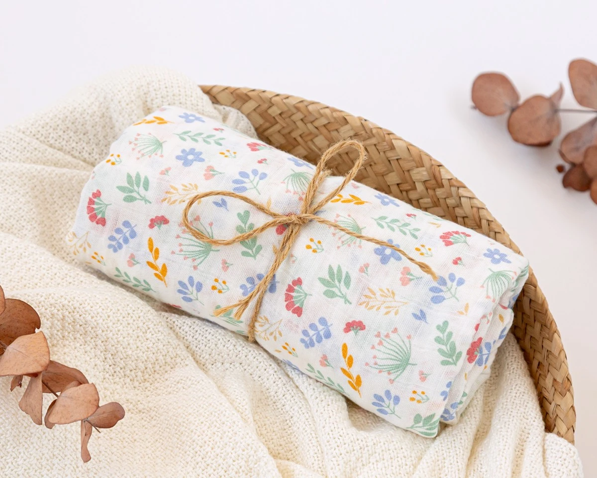 Manta enrolada com padrão floral amarrada com cordão numa cesta de vime