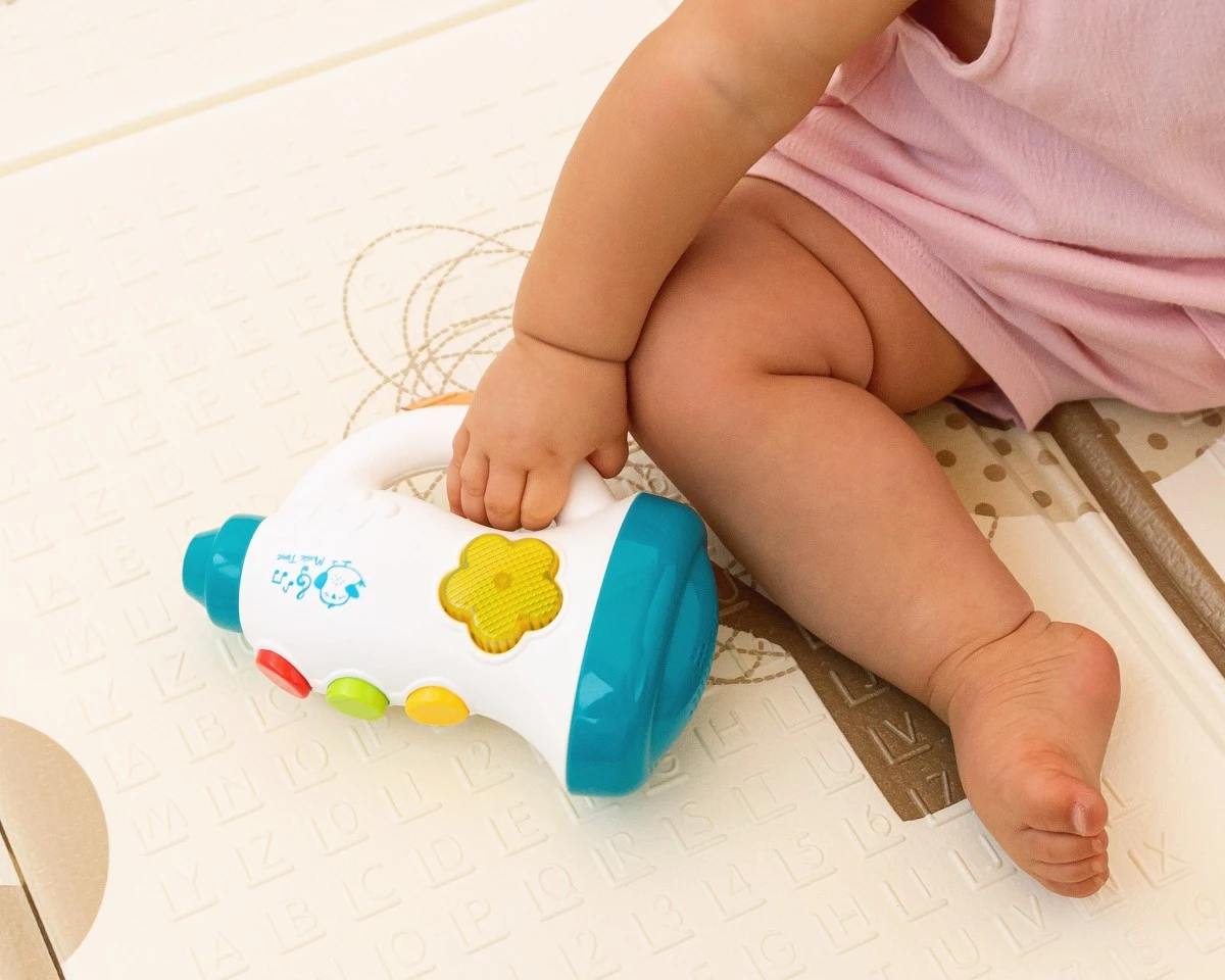 Brinquedo infantil colorido em forma de megafone com bebé sentado no tapete educativo