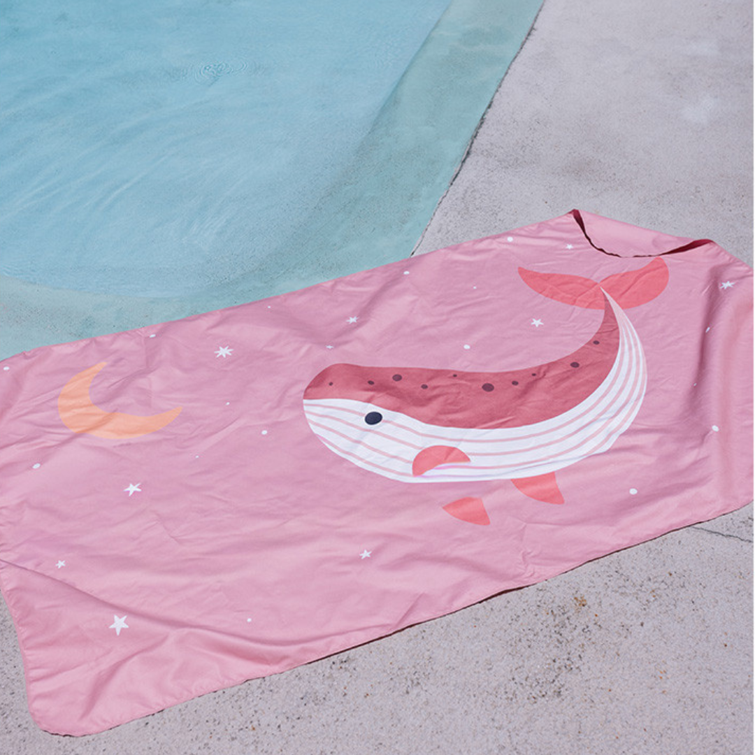Toalha cor-de-rosa com desenho de baleia, estrelas e lua ao lado de piscina