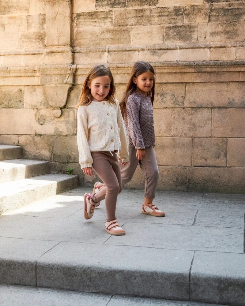 Duas meninas com roupa de malha e calças justas a caminhar numa rua de pedra