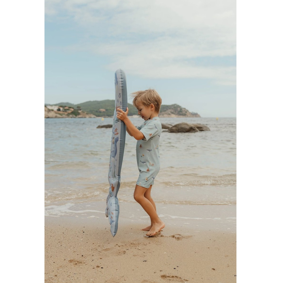 Menino com fato de banho azul segurando brinquedo insuflável azul na praia