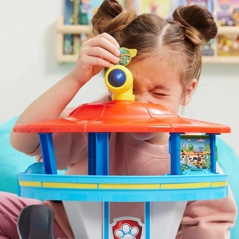 Menina a brincar com torre de brinquedo colorida azul, laranja e amarelo com símbolo de pata