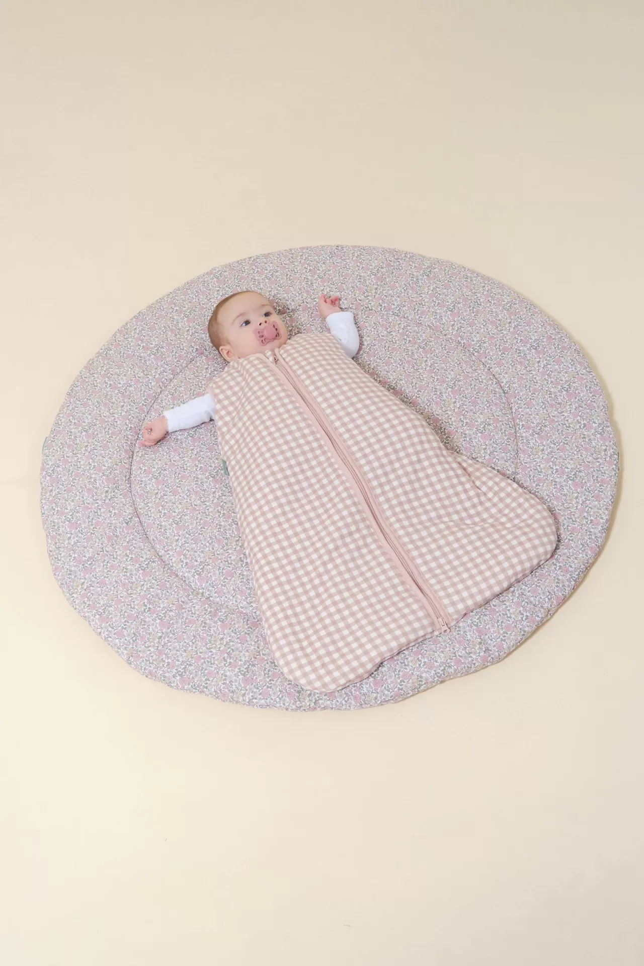 Bebé com saco de dormir rosa de padrão xadrez sobre tapete floral redondo