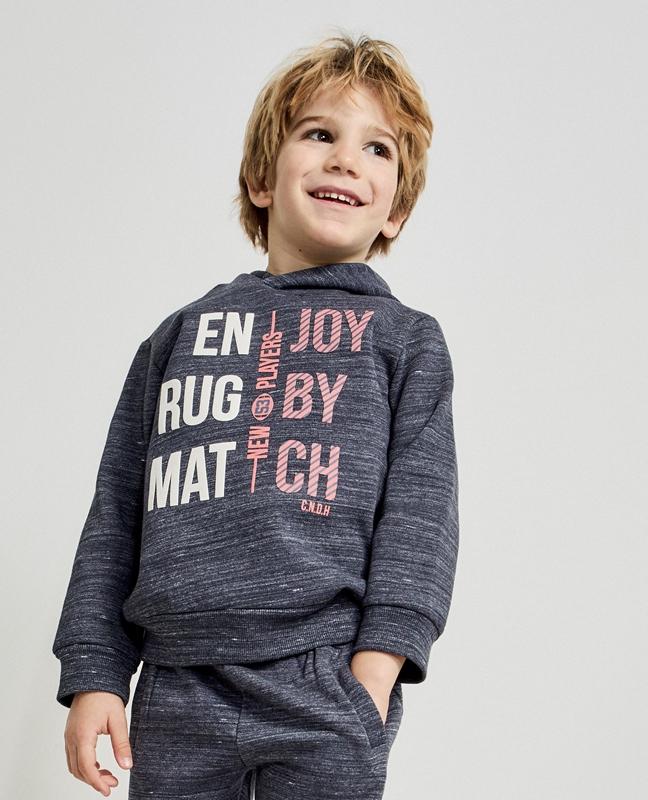 Menino de cabelo loiro com sweatshirt cinza escuro com estampado branco e rosa