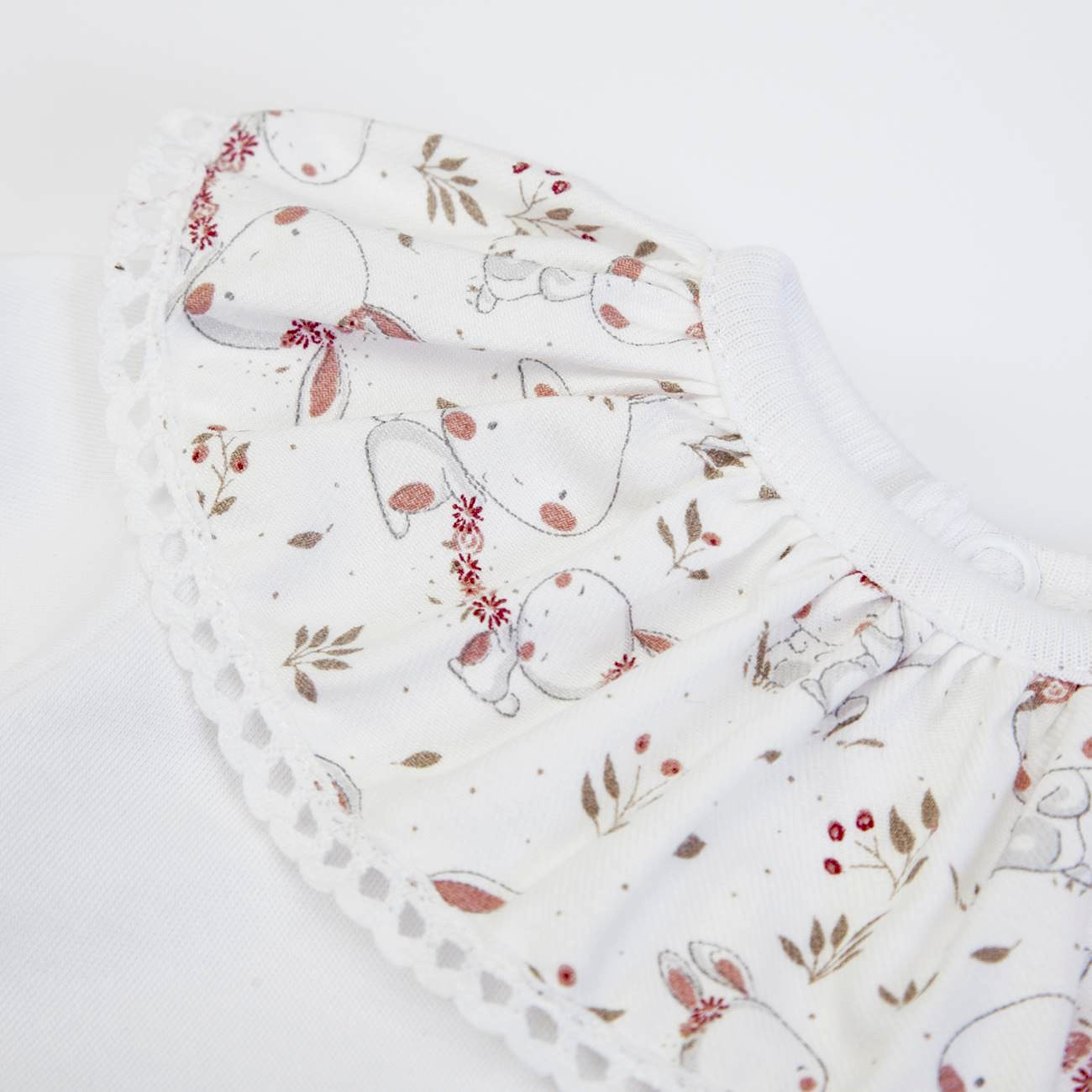Babygrow branco com gola rodada estampada com coelhos e flores em tons suaves, acabamento em renda