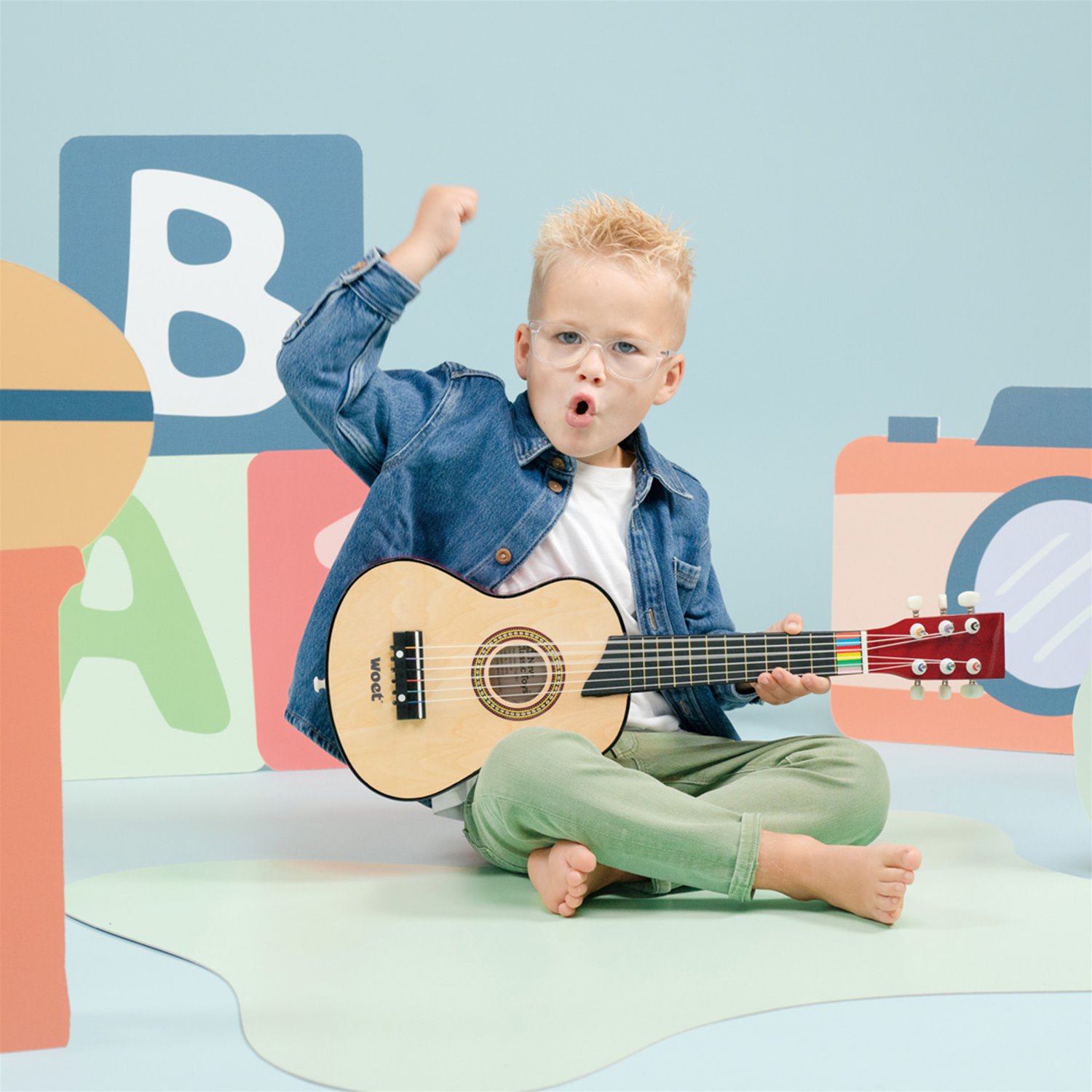 Menino sentado no chão a tocar guitarra em cenário colorido infantil