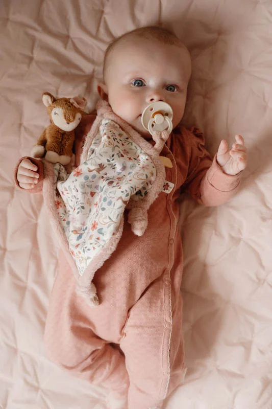 Bebé deitado com fato rosa e chupeta bege segurando brinquedo de peluche