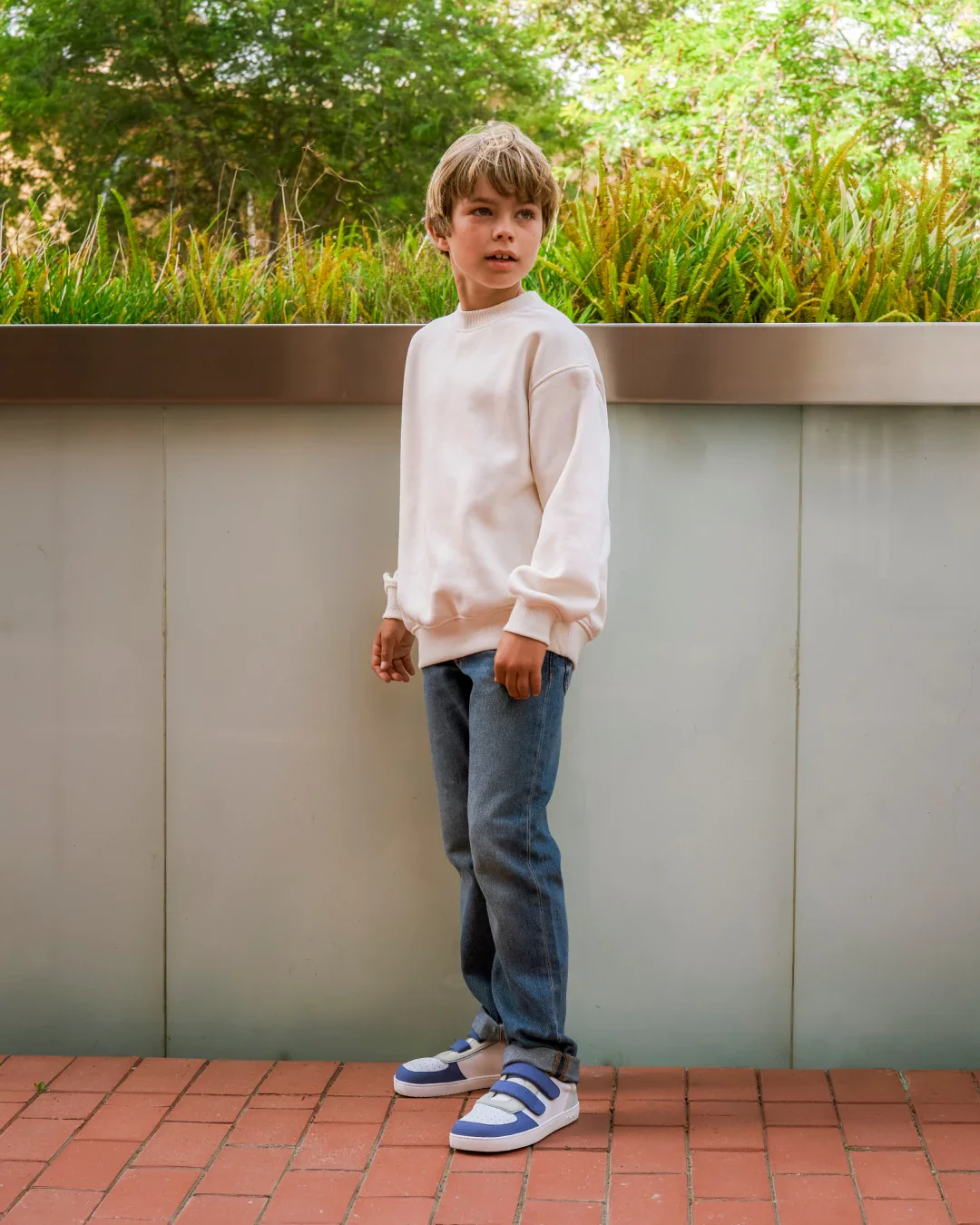 Criança com roupa casual e sapatilhas em ambiente exterior urbano.