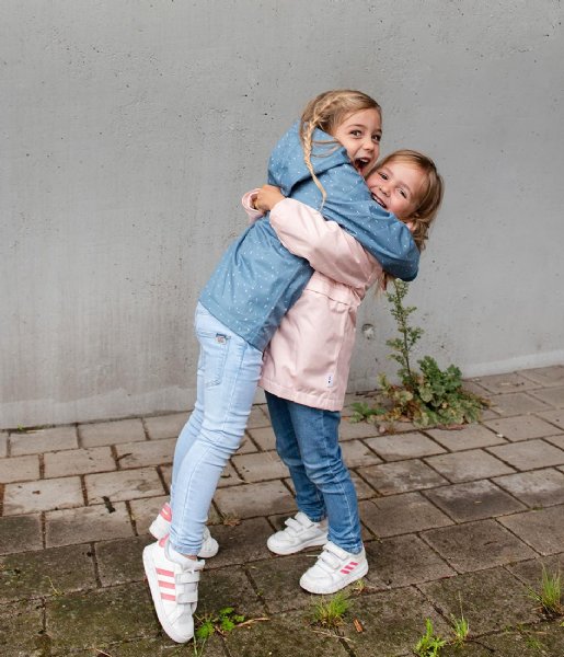 Duas crianças abraçadas na rua, uma com casaco azul e jeans claros e outra com casaco rosa e calças azuis.