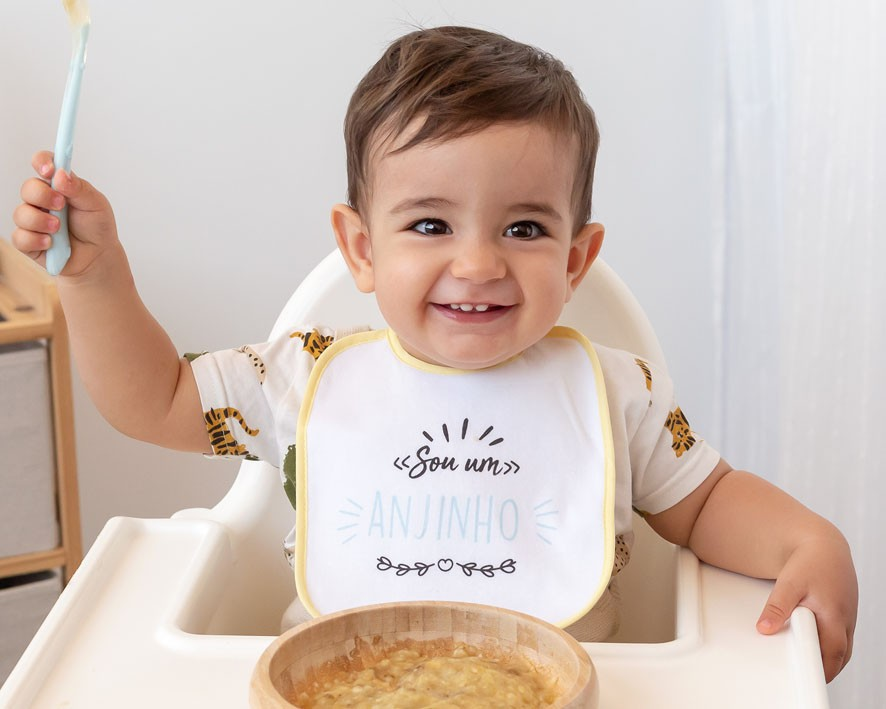 Bebé com babete sentado em cadeira alta com comida