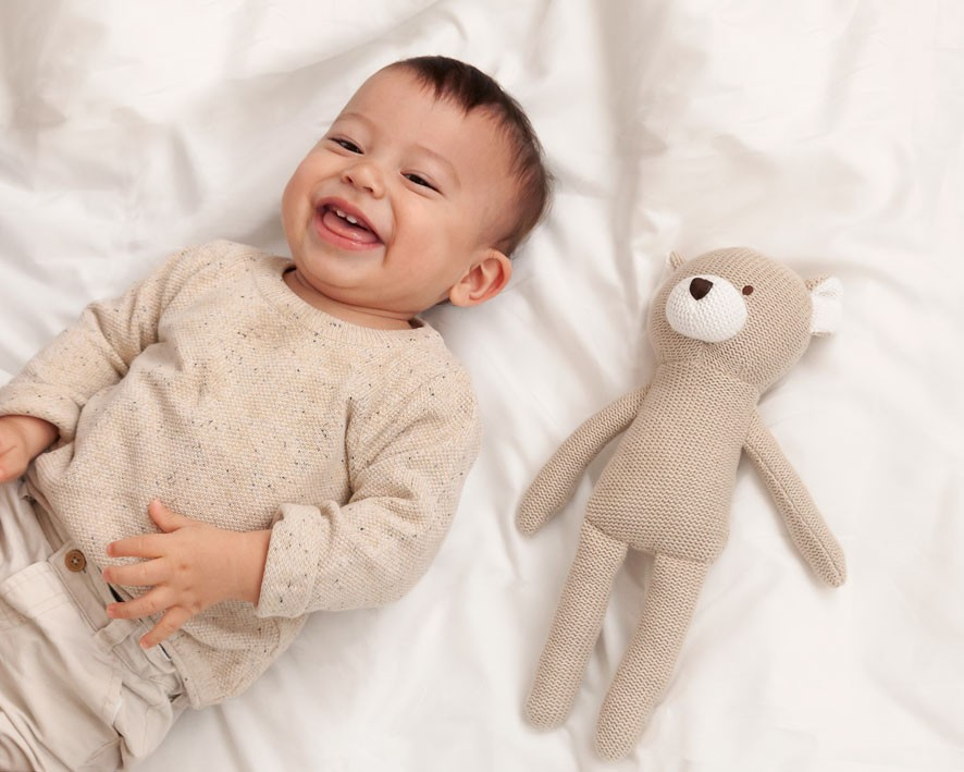 Criança sorridente deitada com boneco de peluche tricotado ao lado