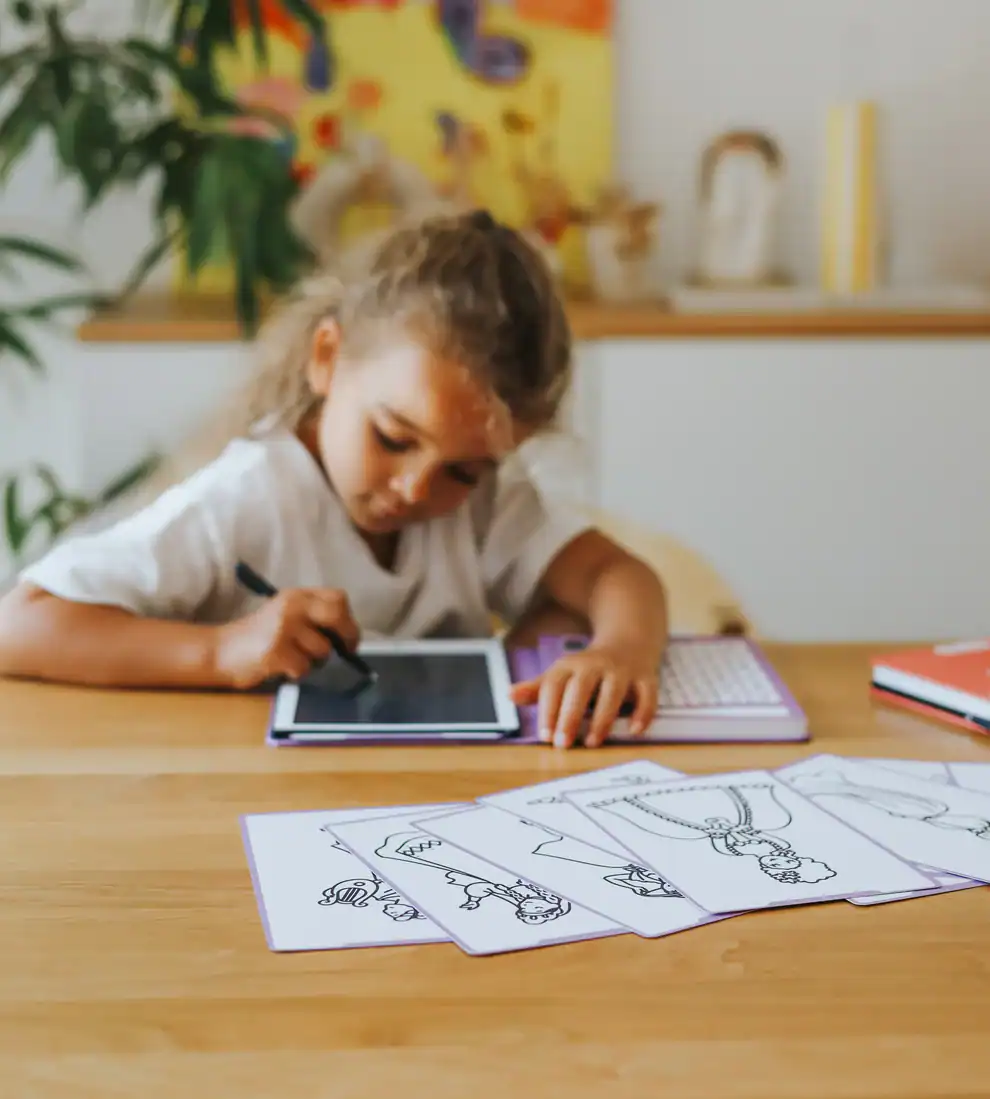 Criança a desenhar num tablet com folhas de desenhos sobre mesa de madeira