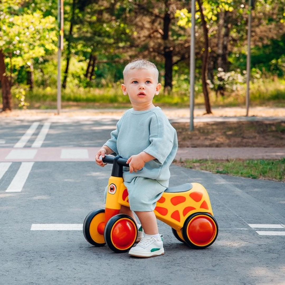 Criança numa mota de brinquedo amarela com detalhes laranja e rodas vermelhas num parque