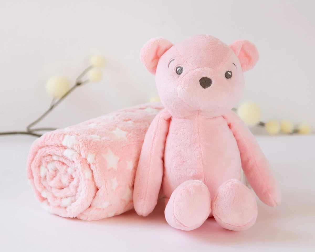 Ursinho de peluche cor-de-rosa e manta com estrelas brancas enrolada sobre superfície branca