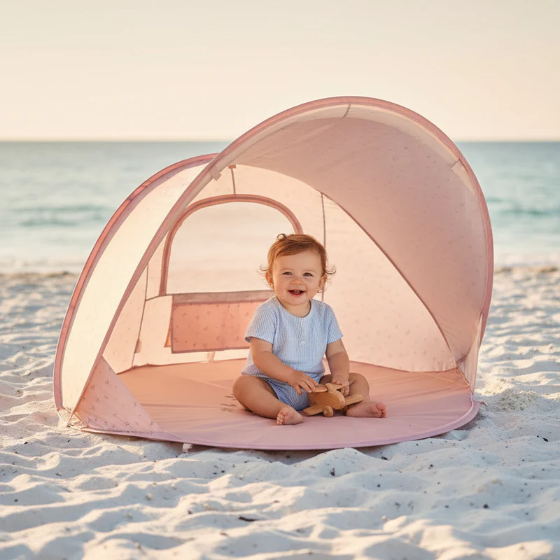 Bebé a sorrir sentado dentro de tenda rosa de praia em areia branca
